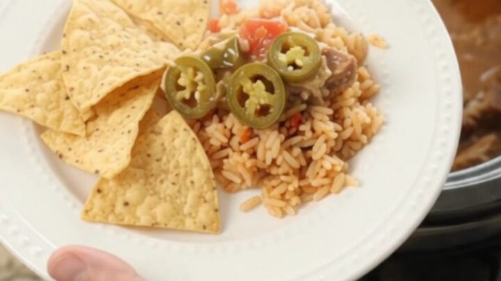 Slow cooker pork carnitas with melted cheese and tomatoes, served in a black crockpot.