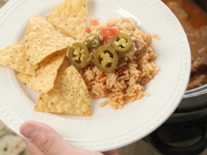 Slow cooker pork carnitas with melted cheese and tomatoes, served in a black crockpot.