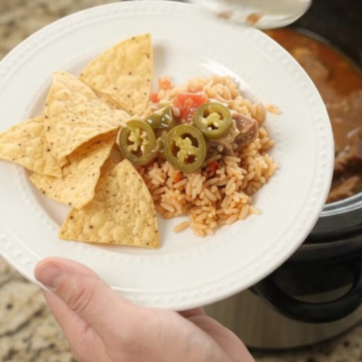 Slow cooker pork carnitas with melted cheese and tomatoes, served in a black crockpot.