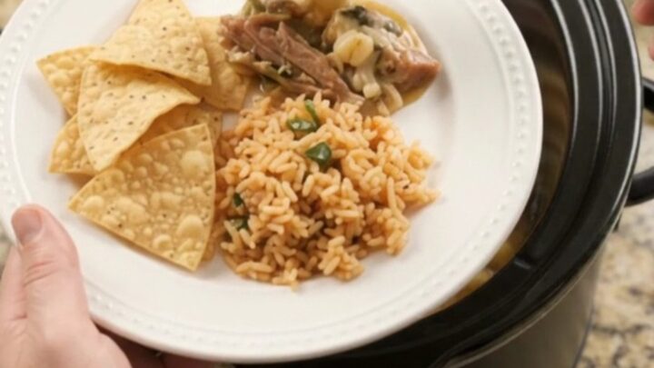 A slow cooker filled with creamy pepper jack pork carnitas, topped with melted cheese and hominy.