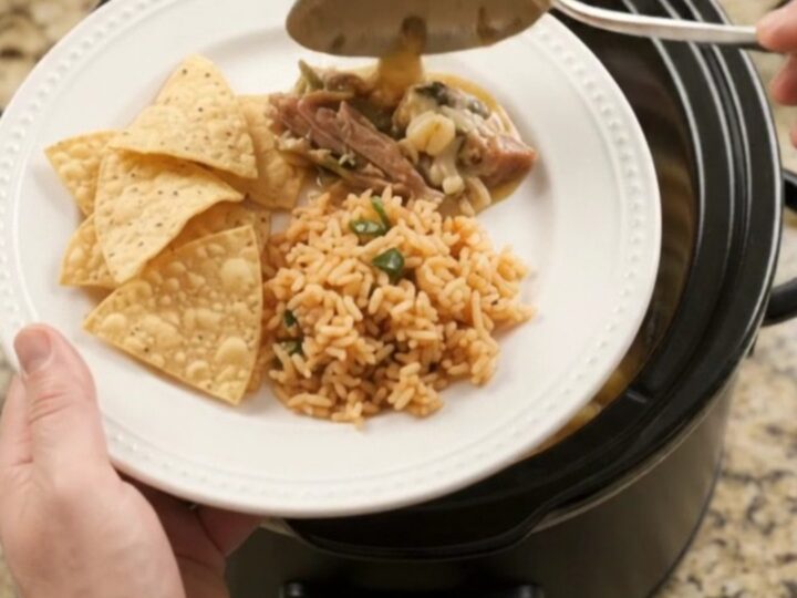 A slow cooker filled with creamy pepper jack pork carnitas, topped with melted cheese and hominy.
