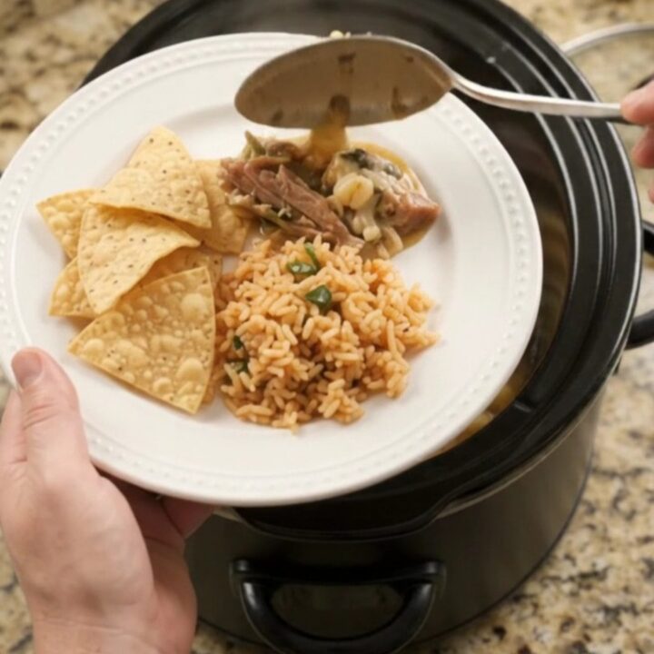 A slow cooker filled with creamy pepper jack pork carnitas, topped with melted cheese and hominy.