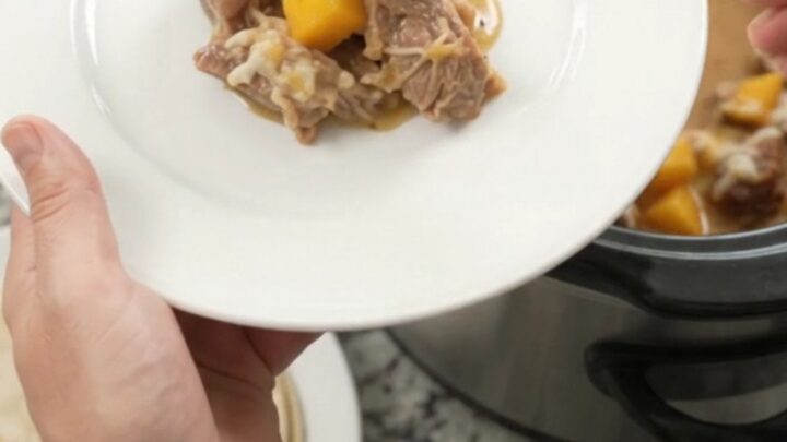 Slow cooker filled with creamy mango habanero pork carnitas, topped with melted cheese and cilantro