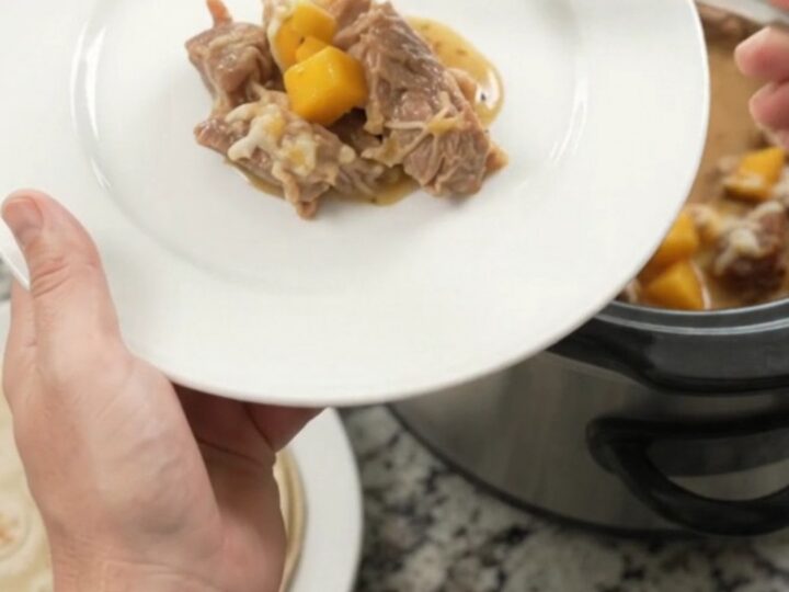 Slow cooker filled with creamy mango habanero pork carnitas, topped with melted cheese and cilantro