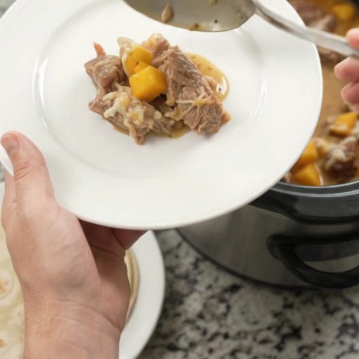 Slow cooker filled with creamy mango habanero pork carnitas, topped with melted cheese and cilantro