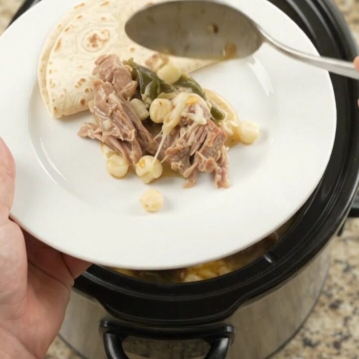 Creamy pork carnitas with hominy and poblano in a slow cooker, topped with melted cheese and steam rising.