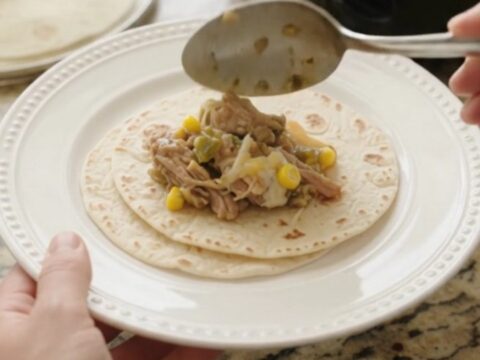 Slow cooker filled with creamy pork carnitas, corn, and green chiles, with melted cheese