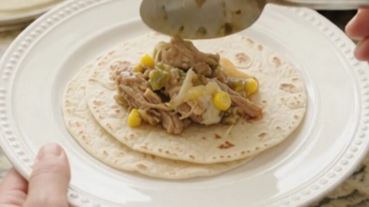 Slow cooker filled with creamy pork carnitas, corn, and green chiles, with melted cheese