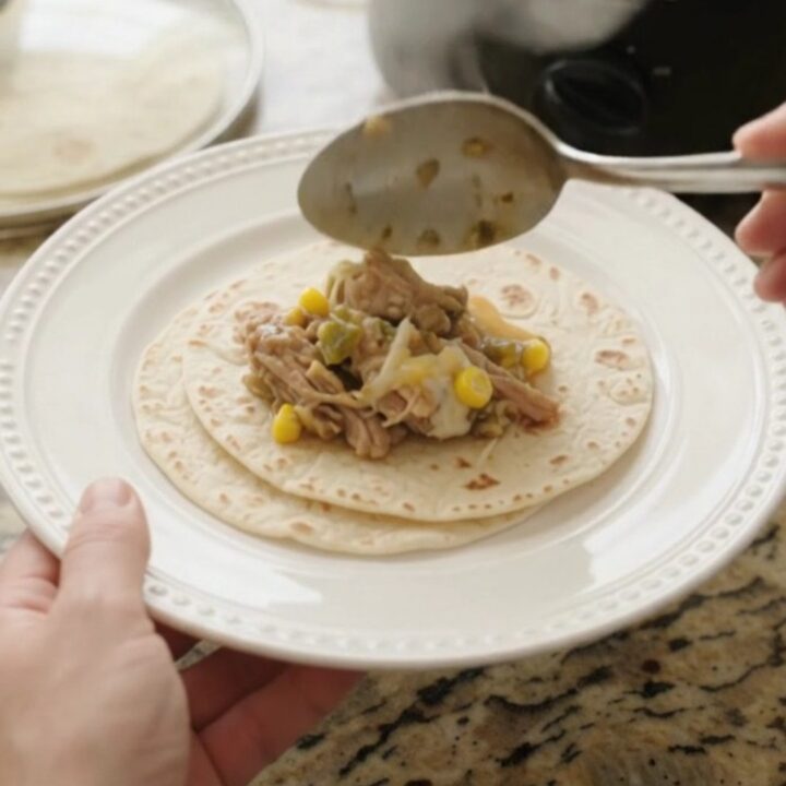 Slow cooker filled with creamy pork carnitas, corn, and green chiles, with melted cheese