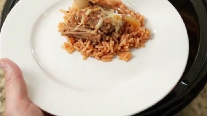 Creamy cheddar and green chile pork carnitas in a slow cooker, topped with melted cheese and corn.