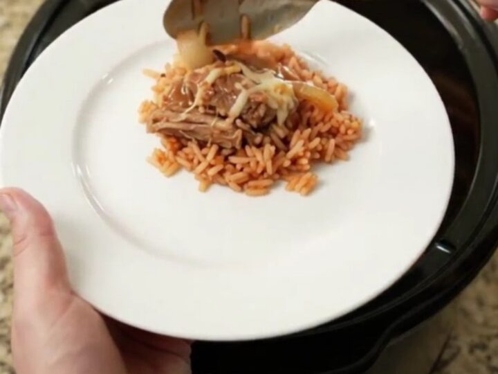 Creamy cheddar and green chile pork carnitas in a slow cooker, topped with melted cheese and corn.