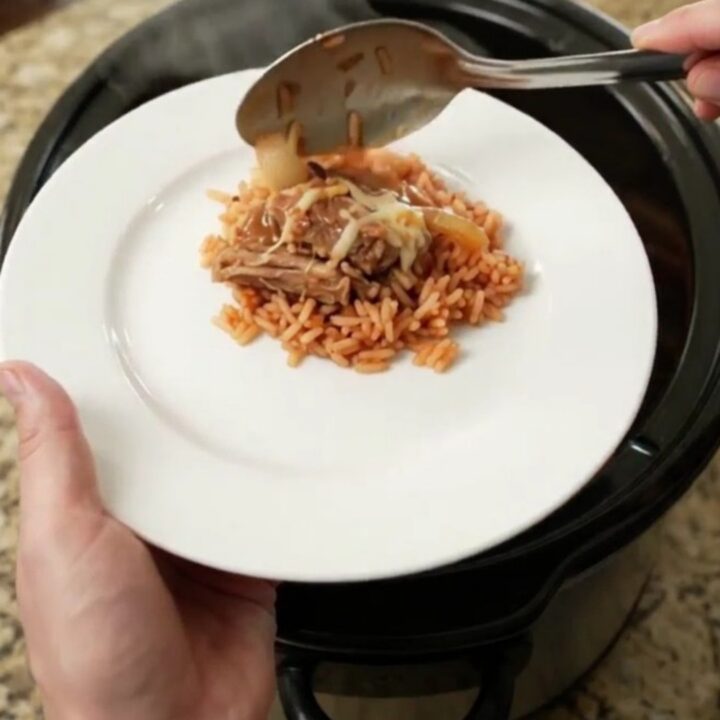 Creamy cheddar and green chile pork carnitas in a slow cooker, topped with melted cheese and corn.