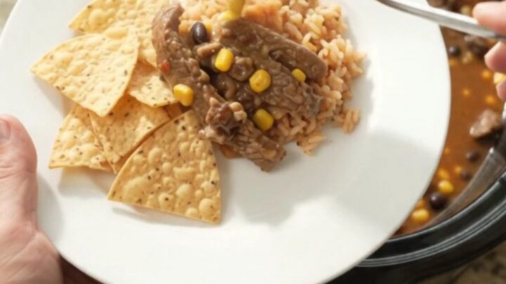 Slow cooker filled with tender skirt steak, black beans, corn, and melted pepper jack queso sauce