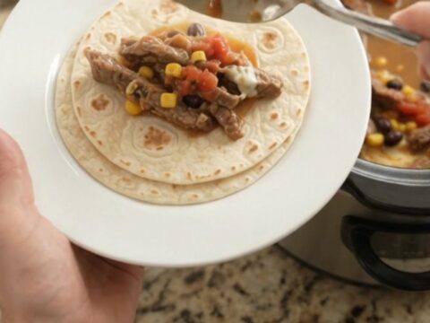 Slow cooker filled with bubbling skirt steak, black beans, corn, and melted cheese sauce.