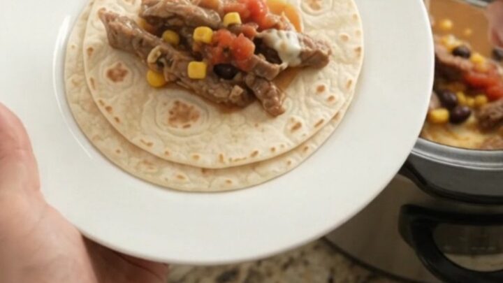 Slow cooker filled with bubbling skirt steak, black beans, corn, and melted cheese sauce.