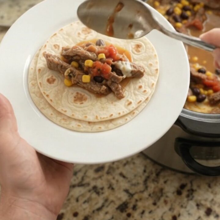 Slow cooker filled with bubbling skirt steak, black beans, corn, and melted cheese sauce.