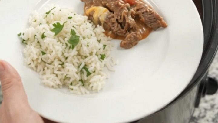 Slow cooker filled with tender skirt steak strips in creamy red enchilada sauce with melted cheddar and pinto beans