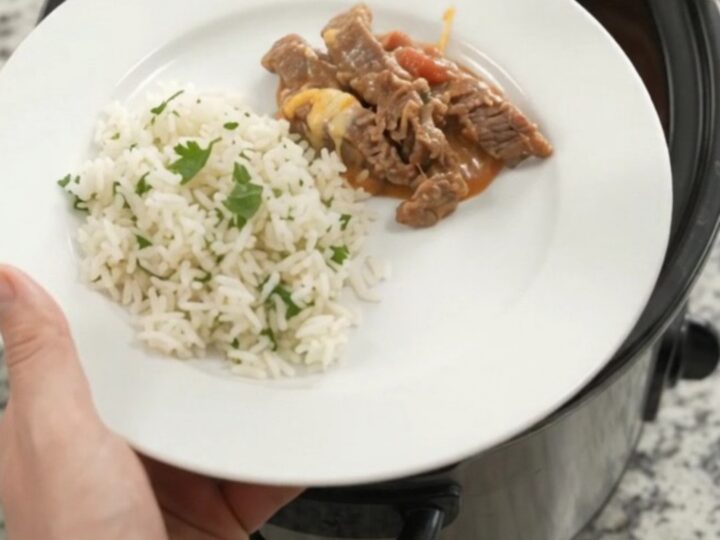 Slow cooker filled with tender skirt steak strips in creamy red enchilada sauce with melted cheddar and pinto beans