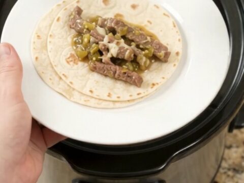 Slow cooker filled with shredded skirt steak in creamy salsa verde sauce, topped with melted cheese.