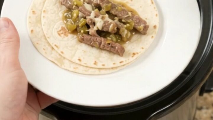 Slow cooker filled with shredded skirt steak in creamy salsa verde sauce, topped with melted cheese.