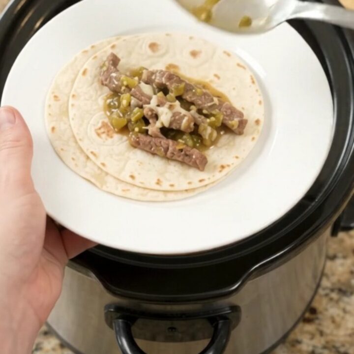 Slow cooker filled with shredded skirt steak in creamy salsa verde sauce, topped with melted cheese.