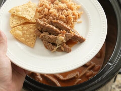Bubbling Crockpot of pepper jack red enchilada skirt steak with melted cheese and sauce