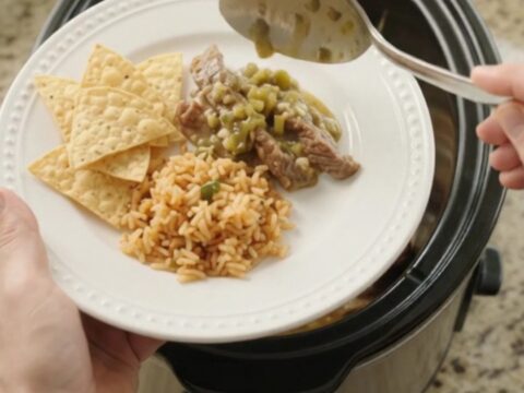 Slow cooker filled with tender skirt steak strips in a creamy green salsa and melted cheese sauce, with steam rising.