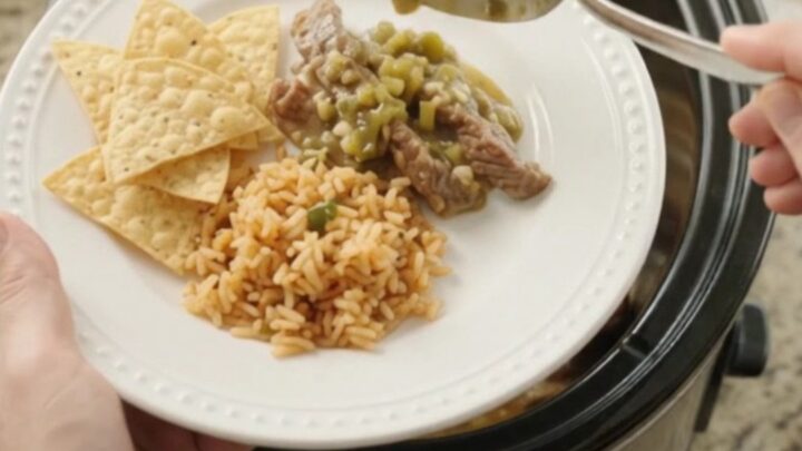 Slow cooker filled with tender skirt steak strips in a creamy green salsa and melted cheese sauce, with steam rising.