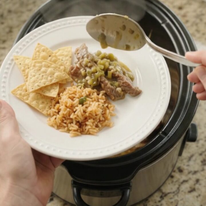 Slow cooker filled with tender skirt steak strips in a creamy green salsa and melted cheese sauce, with steam rising.
