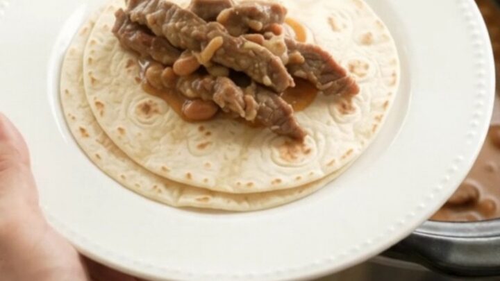 Slow cooker filled with tender skirt steak strips in creamy red enchilada sauce with pinto beans and melted Monterey Jack.