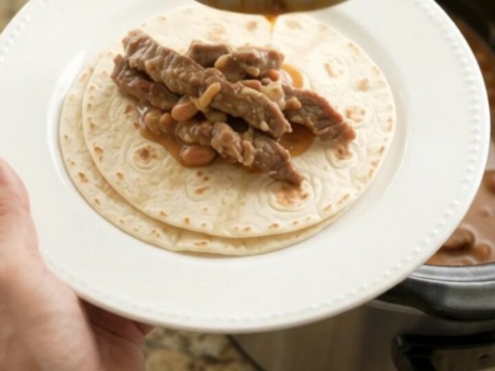 Slow cooker filled with tender skirt steak strips in creamy red enchilada sauce with pinto beans and melted Monterey Jack.