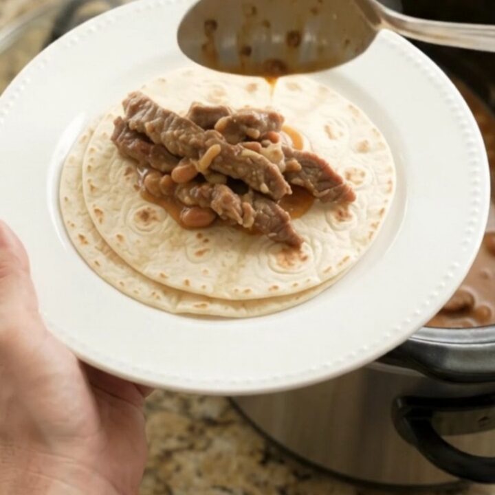 Slow cooker filled with tender skirt steak strips in creamy red enchilada sauce with pinto beans and melted Monterey Jack.