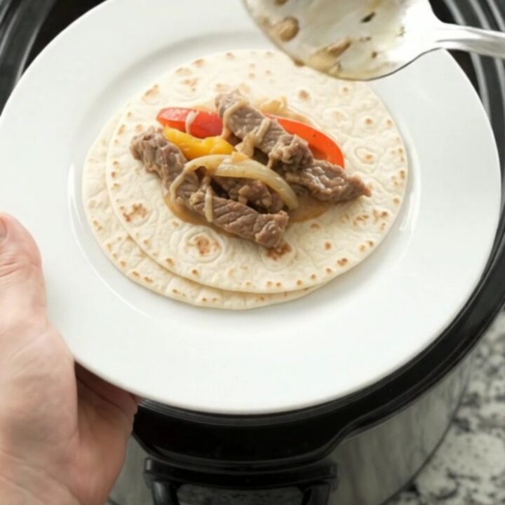 Slow cooker fajita skirt steak with peppers and creamy cheese sauce in a black crock