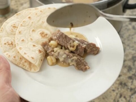 Slow-cooker skirt steak with creamy poblano hominy sauce in a black crockpot.