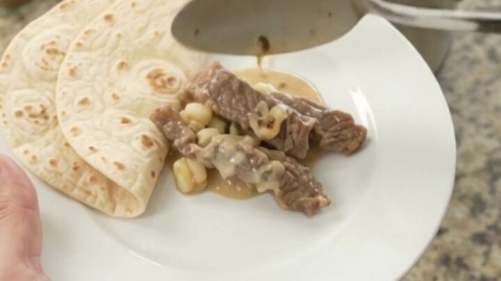 Slow-cooker skirt steak with creamy poblano hominy sauce in a black crockpot.