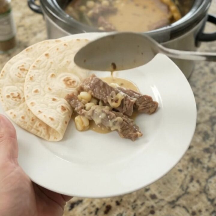 Slow-cooker skirt steak with creamy poblano hominy sauce in a black crockpot.