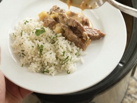 Slow cooker full of creamy cheddar poblano hominy steak, topped with melted cheese and steam rising.