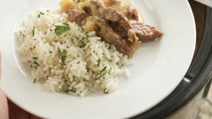 Slow cooker full of creamy cheddar poblano hominy steak, topped with melted cheese and steam rising.