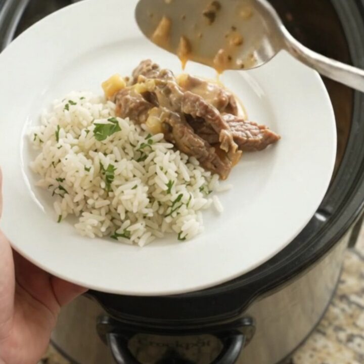 Slow cooker full of creamy cheddar poblano hominy steak, topped with melted cheese and steam rising.