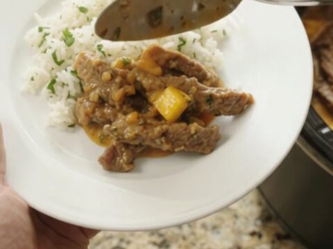 Slow cooker filled with shredded skirt steak in a creamy mango cheddar sauce, topped with cilantro.