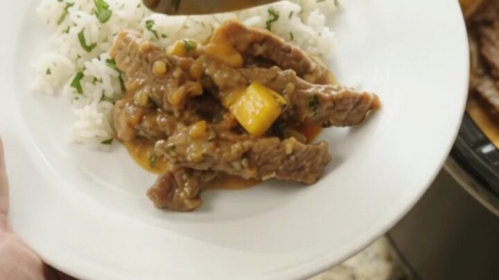 Slow cooker filled with shredded skirt steak in a creamy mango cheddar sauce, topped with cilantro.