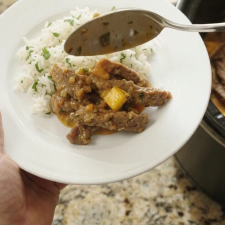 Slow cooker filled with shredded skirt steak in a creamy mango cheddar sauce, topped with cilantro.