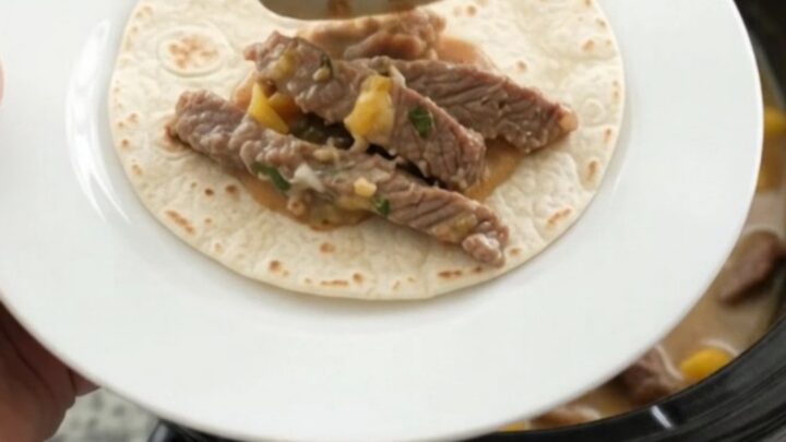 Slow cooker filled with shredded beef in creamy mango habanero sauce, topped with melted cheese and cilantro.