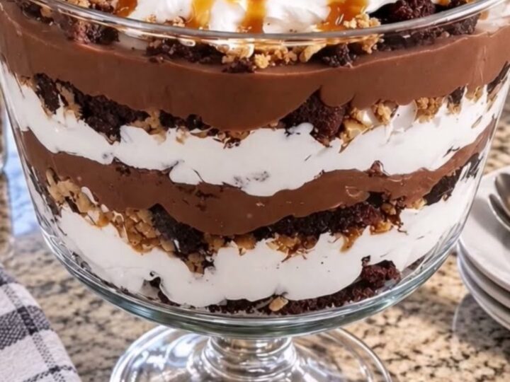 A glass trifle bowl filled with layers of brownies, chocolate pudding, caramel, and whipped cream