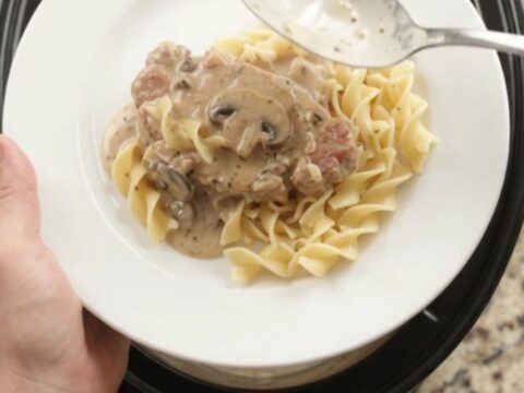 Crockpot sour cream ranch mushroom pork chops in a slow cooker, creamy gravy bubbling