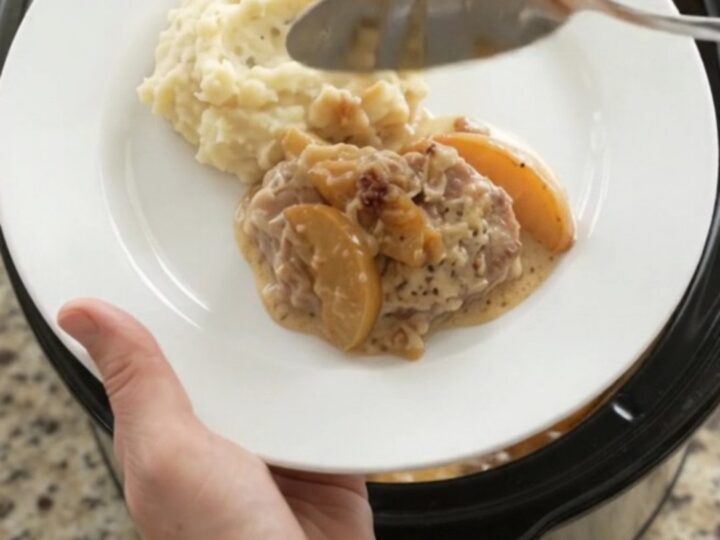 Crockpot full of tender pork chops with apples and creamy Gruyère sauce, bubbling and glistening.