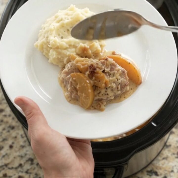 Crockpot full of tender pork chops with apples and creamy Gruyère sauce, bubbling and glistening.