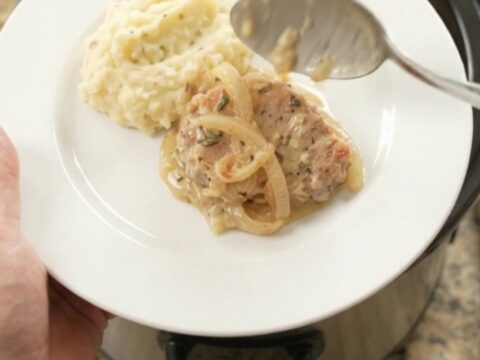 Crockpot full of tender pork chops in a creamy onion and Gruyère sauce, with steam rising.
