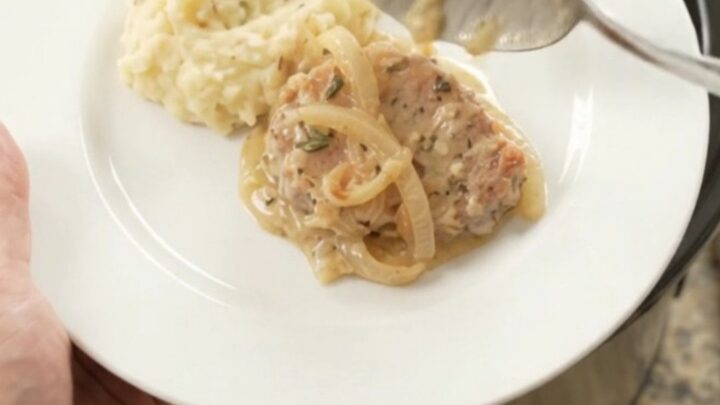 Crockpot full of tender pork chops in a creamy onion and Gruyère sauce, with steam rising.
