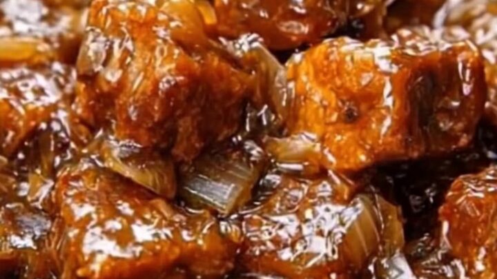 Slow-cooker honey garlic beef tips with a glossy, dark sauce and onions in a ceramic serving dish.